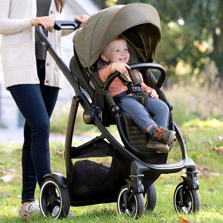 Mum pushing Graco® Evo® XT over grass as little boy rides in the pushchair 