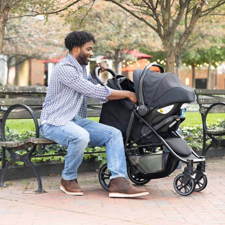 Dad in park with baby in Graco EeZefold travel system. 